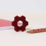 Globus aus roten Perlen, daneben ein Lernbuch und ein Bleistift mit Tiermuster auf weißem Hintergrund.