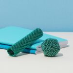 Glitzernde grüne Schmuckperlen in verschiedenen Formen, die auf blauen Notizbüchern und einem hellblauen Hintergrund liegen.