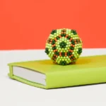 Bedeutungsvoller Beadball geformt wie eine Blume, auf einem grünen Buch gelegen, vor orangefarbenem Hintergrund.