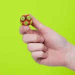 2. Bunte, kugelförmige Murmeln, die eine kleine Figur darstellen, die von einer Hand gehalten wird, vor einem hellgrünen Hintergrund.