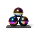 Leuchtende Kugeln mit Irisierenden Oberflächen, die auf einer schwarzen Basis stehen, erzeugen einen reflektierenden, schimmernden Effekt. Die farbigen Metallkugeln sind ein modernes dekoratives Element für Design und Kunst.