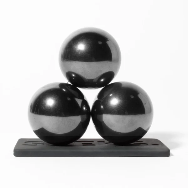 Glänzende schwarze Murmel-Kugeln, die auf einer schwarzen Plattform in einer scheinbar ausgewogenen Pyramide angeordnet sind. Schwarz-Weiß-Fotografie mit hohem Kontrast und klaren Reflexionen.