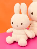 Weißer Plüschteddy im Miffy-Design mit langen Ohren vor einem orange-pinken Hintergrund.