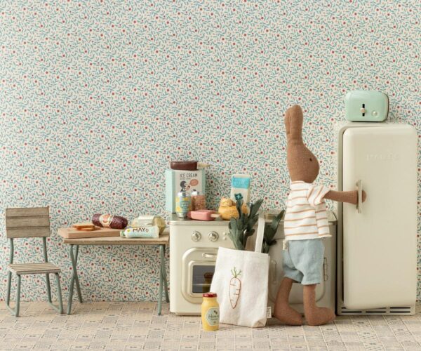 Ein Stoffhund in einem Vintage-Küchenraum, der an eine Küche erinnert, mit Kühlschrank, Waschmaschine und einem kleinen Tisch mit Stühlen.